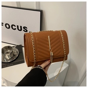 Detailed view of brown crossbody bag featuring V-quilted texture and gold tassel charm