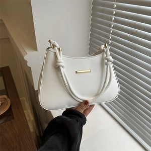 Elegant white semi-circle shoulder bag with knotted handle and gold bar detail on window ledge