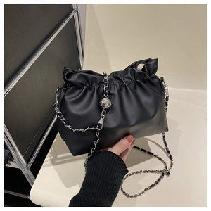 Detail of black pleated bucket bag featuring silver chain strap and decorative metal ball