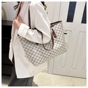 Fashionable printed tote bag with leather trim worn on shoulder by a model in interior setting
