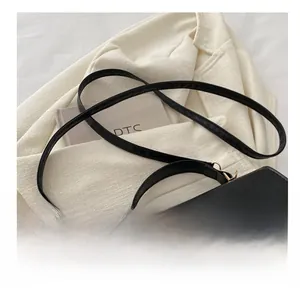 Close-up of a black leather handbag with a gold metal logo and tassel on a beige blazer