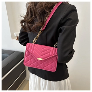 Detail of fuchsia quilted shoulder bag with gold chain strap shown on a model