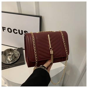 Detail of burgundy crossbody bag with V-quilting, gold chain strap and fringe charm
