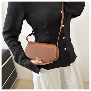 Brown leather saddle bag with gold metal lock worn as a crossbody with casual outfit