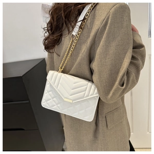 Chic white quilted chain bag with V-shaped embroidery worn by a model in a modern interior