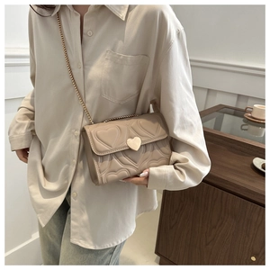 Détail du sac bandoulière beige matelassé avec fermoir cœur doré et bandoulière chaîne