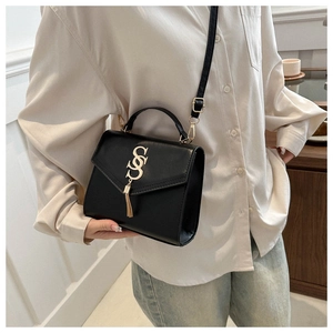 Detail of black crossbody bag featuring a gold SS emblem and stylish metal tassel accent