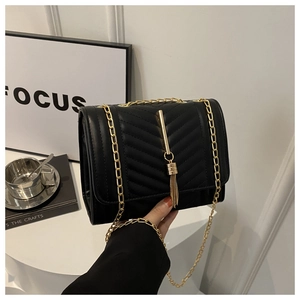 Detail of black V-quilted crossbody bag with golden tassel and metal chain strap