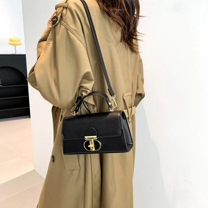 Sac à bandoulière en similicuir noir mat avec boucle dorée porté avec un trench