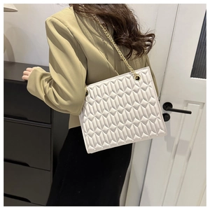Detailed view of white quilted chain shoulder bag worn on a beige blazer back