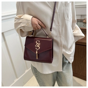 Detail of burgundy flap bag featuring gold double S logo and metal tassel accents