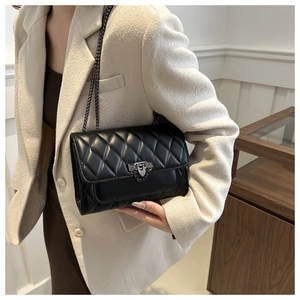 Detail of black quilted leather bag featuring dark grey metal lock and chain strap