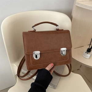 Sac messager vintage en cuir PU marron avec doubles boucles argentées sur une chaise