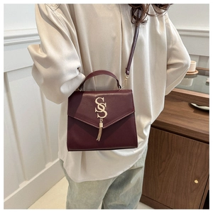 Close-up of wine red leather handbag featuring gold S-shaped lock and metal tassels