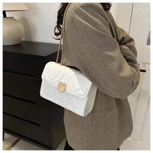Détail du sac bandoulière blanc avec matelassage cœur et chaîne dorée sur un mannequin