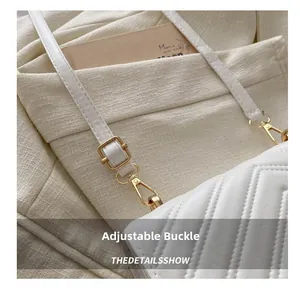 Détail d'une boucle en métal doré et d'une bandoulière en cuir sur un sac blanc épuré
