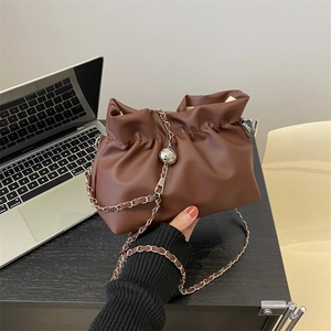 Brown ruched cloud bucket bag with silver chain strap on a desk in a modern office setting