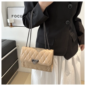 Detail of beige quilted chain shoulder bag with metal lock worn on model's waist