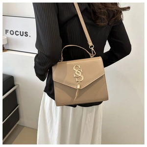 Close-up of khaki leather crossbody bag with gold tassel and logo detail on model