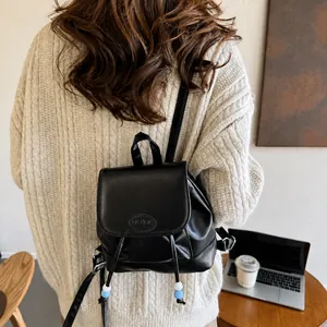 Detalle de mini mochila negra con cuentas de cordón sobre un suéter de punto beige