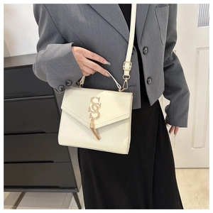 Detail of a beige flap bag featuring a golden S-logo, metallic tassels, and a slim strap
