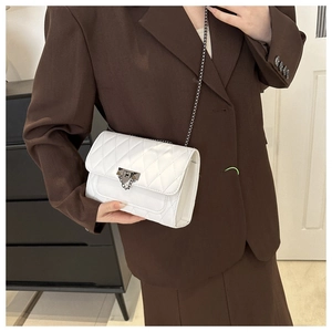 Detail of white quilted leather bag with metallic lock and chain strap on a brown suit
