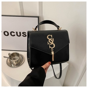 Detail of black faux leather handbag featuring a gold SS logo and metal tassel accent