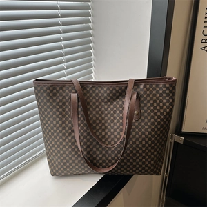 Brown monogram tote bag with leather handles and geometric pattern in a window setting