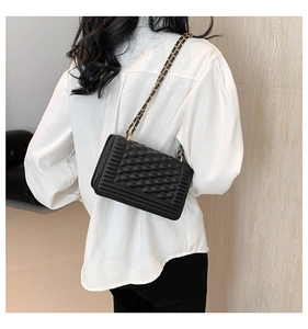 Detail of black textured square crossbody bag with chain strap on white shirt model