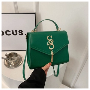Detailed macro view of dark green handbag with golden V-shaped clasp and stylish tassel