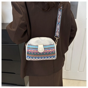 Close-up of bohemian embroidery patterns and wide woven strap on a white crossbody bag