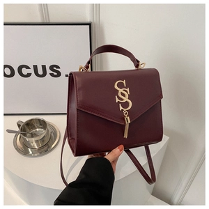 Detail of burgundy leather handbag featuring gold S-logo and stylish hanging fringe tassel