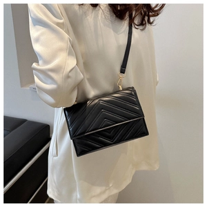Gros plan du sac à bandoulière noir matelassé avec boucles dorées porté par un mannequin