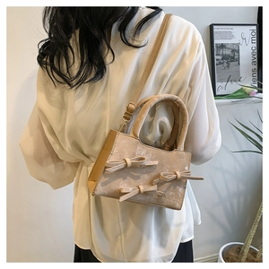 Détail d'un sac bandoulière mat beige avec nœuds décoratifs porté par un mannequin chic