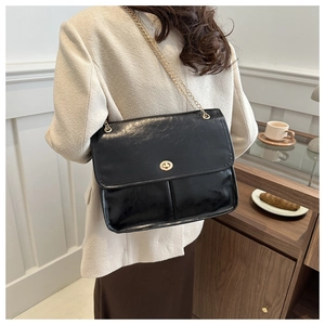 Detail of black faux leather shoulder bag with gold chain strap on beige blazer