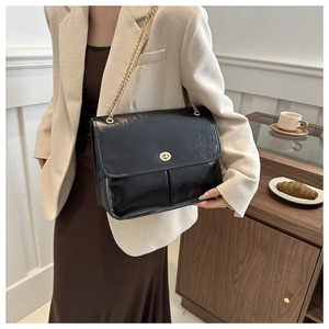 Detail of vintage black shoulder bag with gold chain strap worn by a model in a cafe