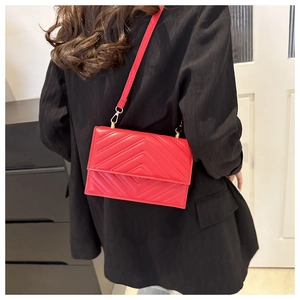 Détail d'un sac bandoulière rouge matelassé en V avec boucles dorées porté sur un blazer