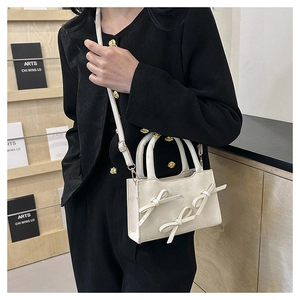 Détail du sac à main crème avec nœuds porté par un mannequin en costume chic