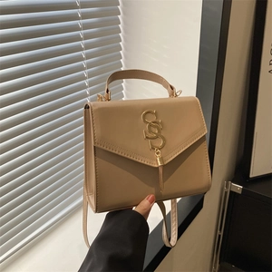 Minimalist beige crossbody bag with SOS metal logo and tassel detail in natural light
