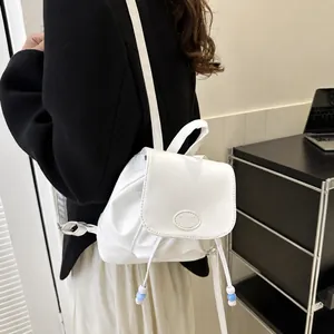 Detalle de una mini mochila de cuero PU blanco con logo de moda y cordón decorativo con cuentas
