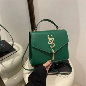 Deep green leather crossbody bag with gold S-logo and fringe on white pedestal