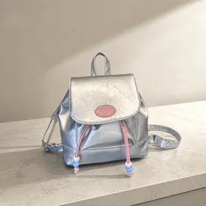 Detalle de mini mochila plateada metalizada con parche de logo rosa y cierre de cordón con cuentas