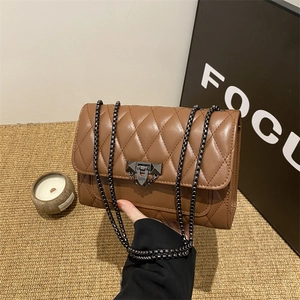 Brown quilted crossbody bag with metal chain strap and turn-lock closure on rustic table