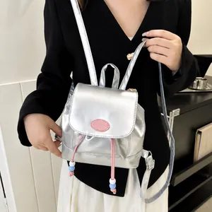 Detalle de mini mochila plateada metalizada con cordón rosa y etiqueta de logo de moda