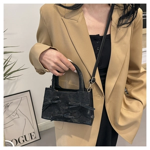 Détail d'un sac à main noir avec nœuds porté par un mannequin en costume élégant