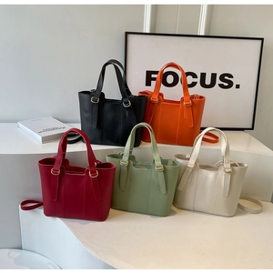 Five assorted colors of textured leather bucket bags displayed on white minimalist steps