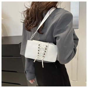 Gros plan d'un sac à bandoulière blanc avec laçage décoratif porté sur un blazer gris