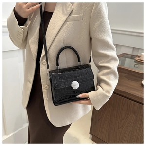 Detail of black faux crocodile skin handbag with silver round metal lock and texture
