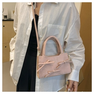 Sac à bandoulière rose mat avec trois nœuds décoratifs porté par un mannequin