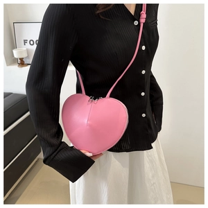 Modèle portant un sac bandoulière rose en forme de cœur avec détail de fermeture éclair